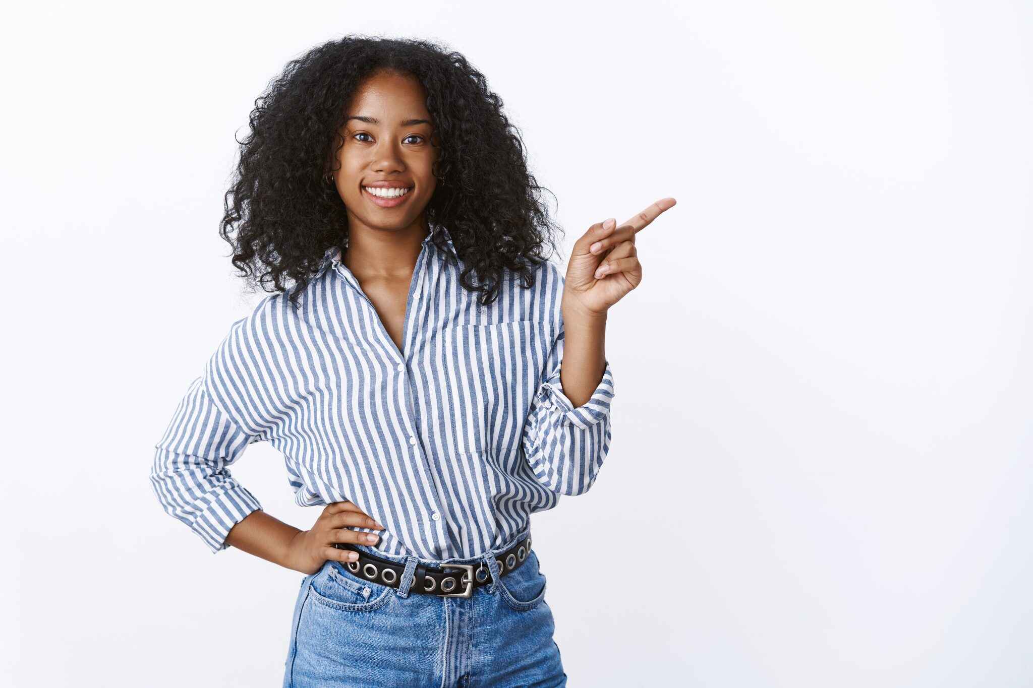 confident good looking outgoing nice dark skinned curly haired female friend suggesting visit cozy cafe pointing sideways inviting come smiling broadly friendly vibe holding hand waist casually 2048x1