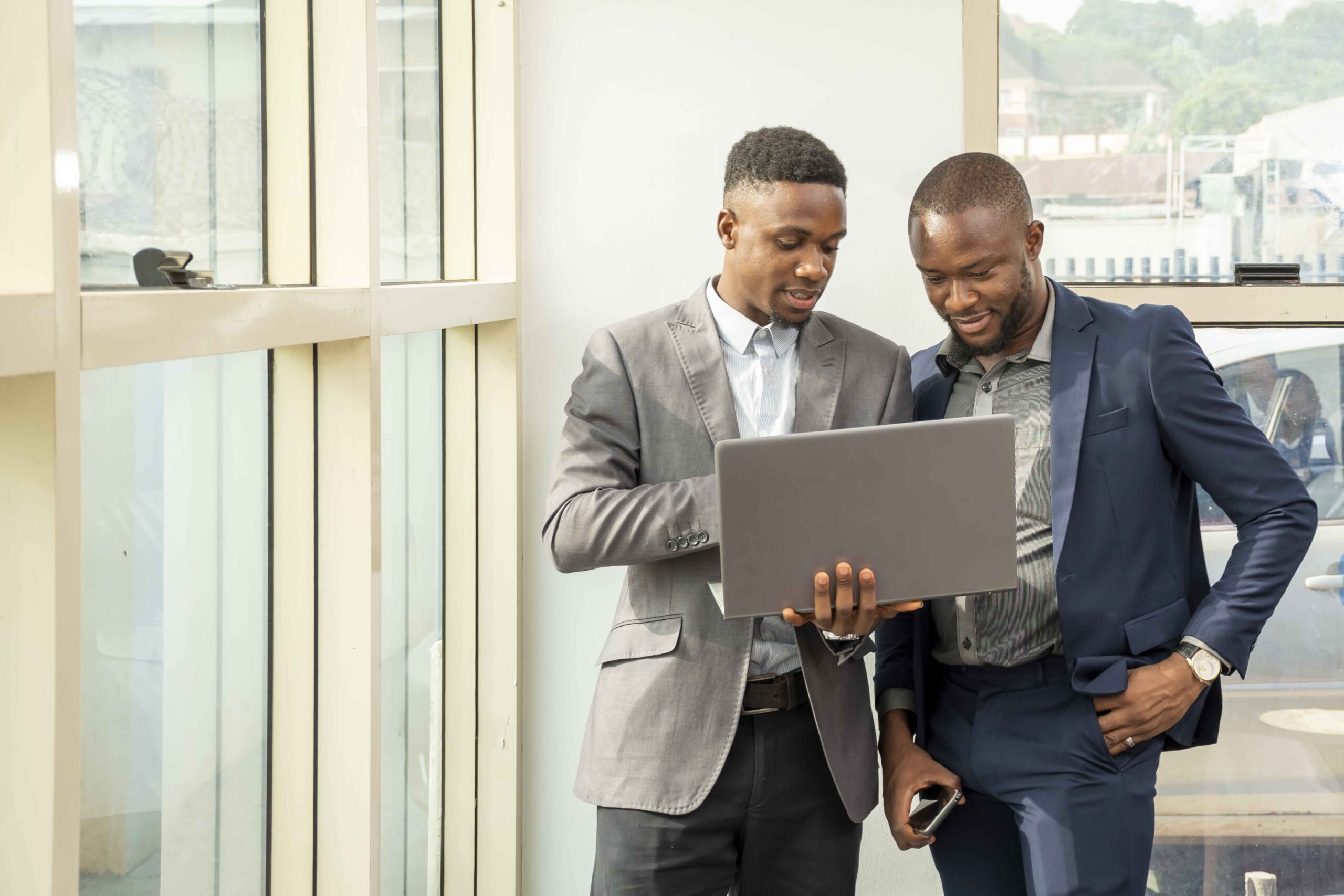 young businessmen standing together holding laptop discussing business (1) (1)